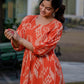 Model in an orange ikkat dress stands gracefully in a landscaped garden, showcasing the flow and pattern of the outfit.
