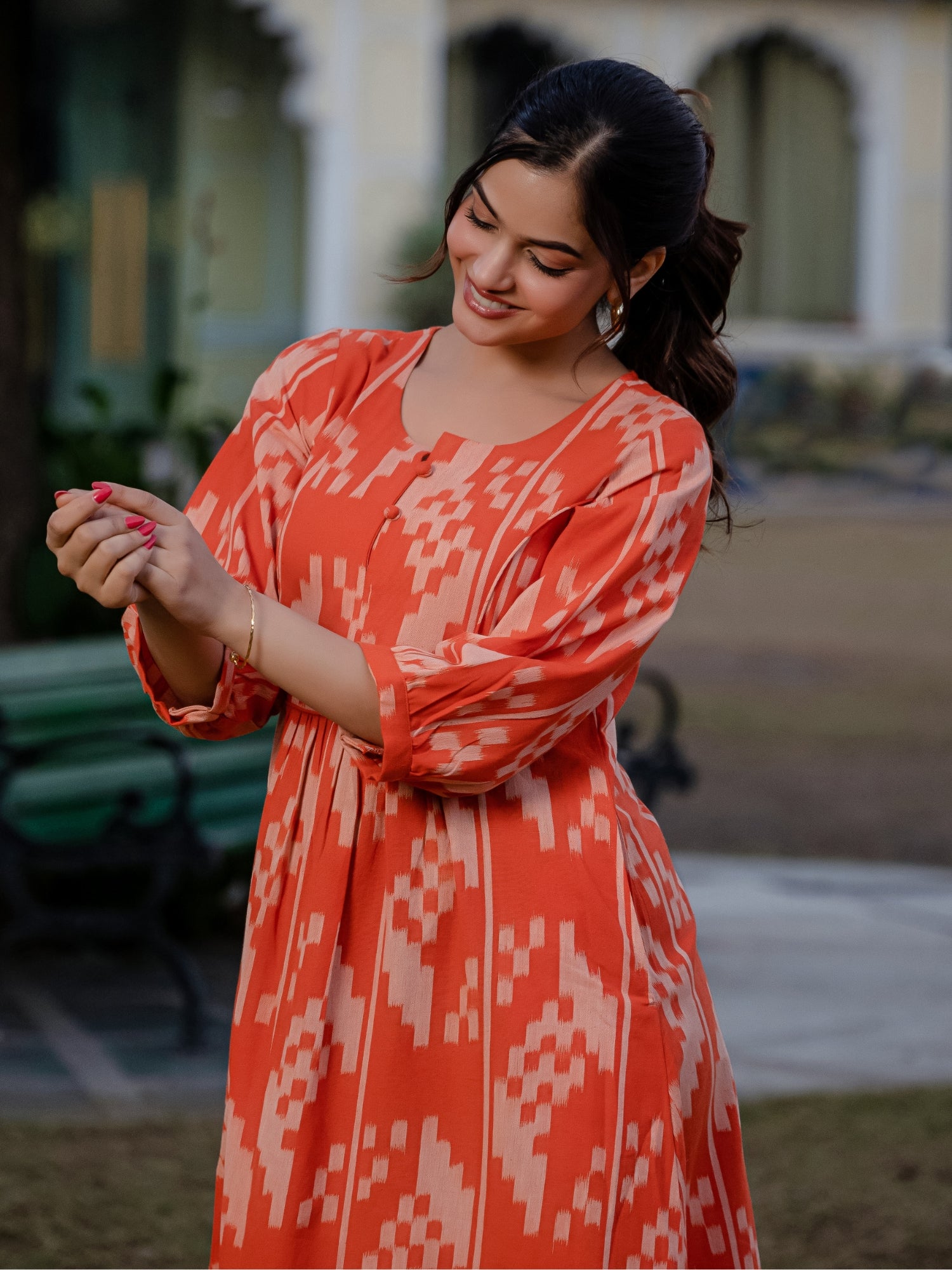 Model in an orange ikkat dress stands gracefully in a landscaped garden, showcasing the flow and pattern of the outfit.