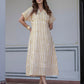 A woman modeling a short-sleeved midi dress with vertical mustard yellow and white stripes, standing in front of a light-colored wall.