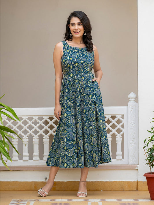 A woman modeling a sleeveless midi dress with a blue and green paisley pattern, standing in front of a white railing and beige wall.