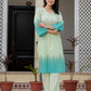 A woman stands outdoors in front of a building entrance wearing a light mint green and turquoise ombre kurta with matching pants.