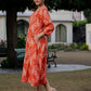 Playful pose of a woman wearing an orange ikkat dress, with the outfit’s flare and print clearly visible in an open garden area.