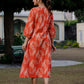 Back view of an orange ikkat midi dress worn by a woman standing outdoors, highlighting the fabric pattern and dress silhouette.
