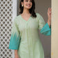 A woman wearing a light mint green V-neck kurta with a teal tie-dye hem and sleeve cuffs, standing in a doorway.